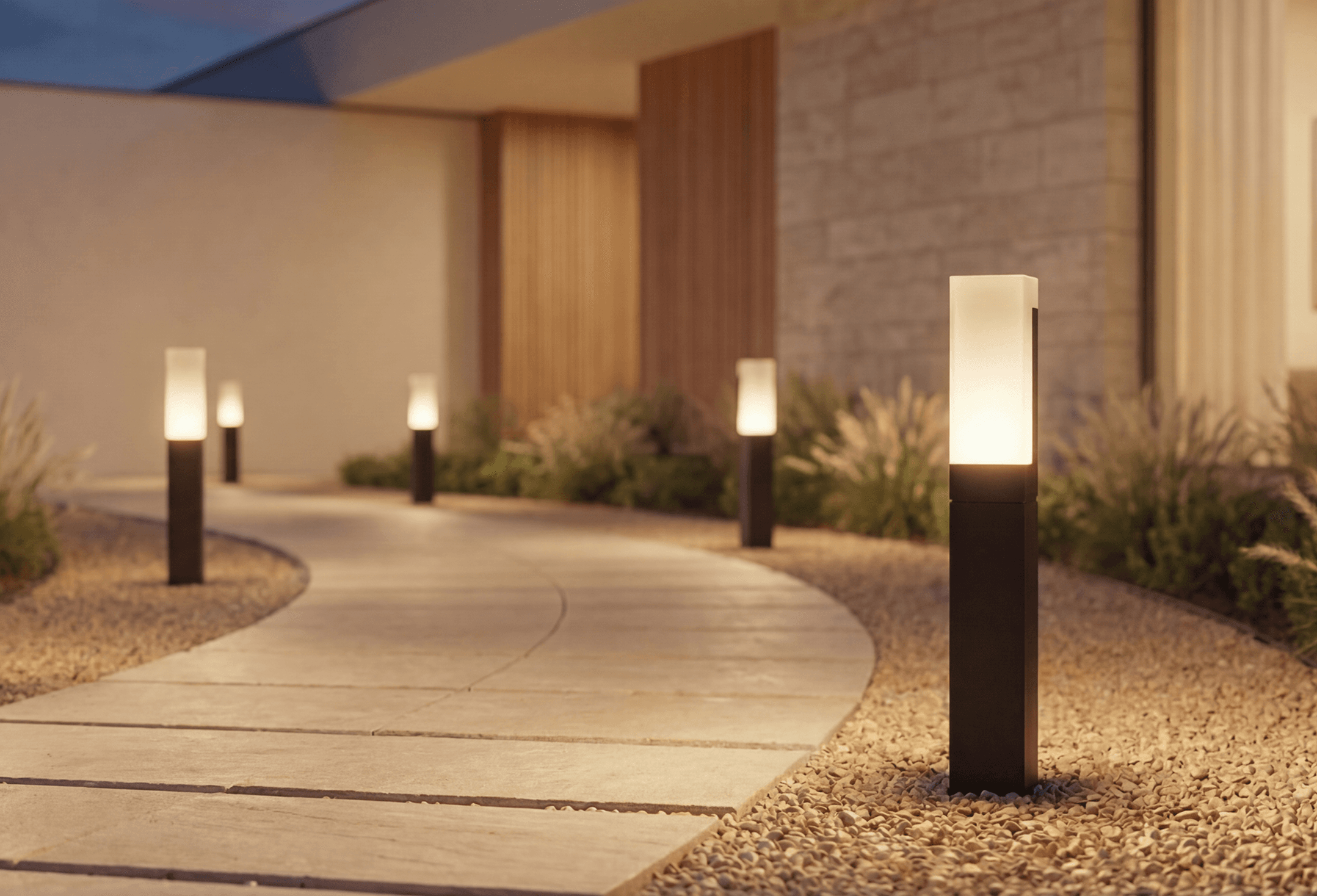 A row of Meadow path lights along a curved stone walkway at dusk