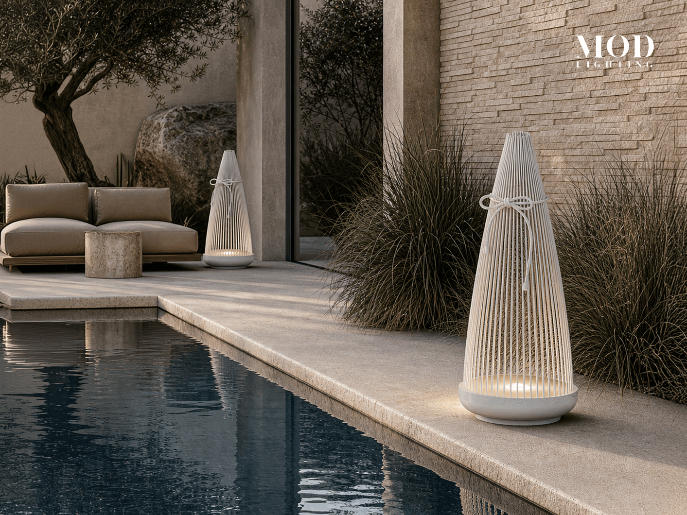 Birch white cone lanterns lit beside a pool and an olive tree on a stone terrace