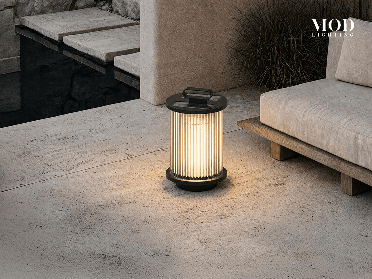 Vesper black portable lantern lit on a stone terrace beside an outdoor sofa and steps
